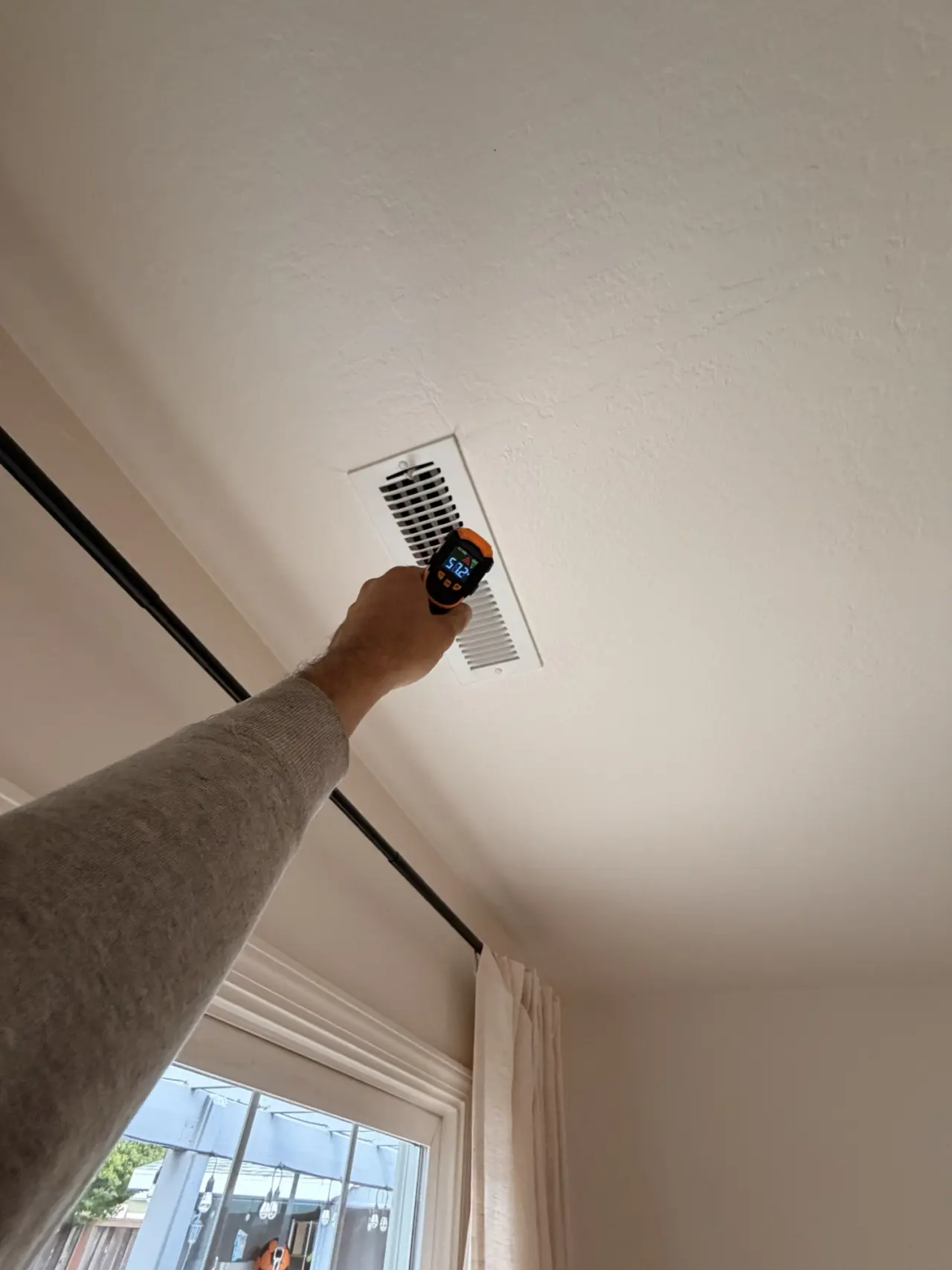 Technician checking supply-air temperature at a ceiling register during the San Mateo heat pump startup