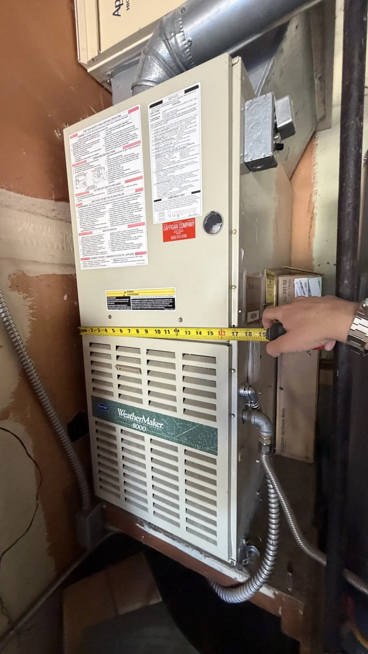 Old Carrier WeatherMaker gas furnace being measured before replacement in San Mateo