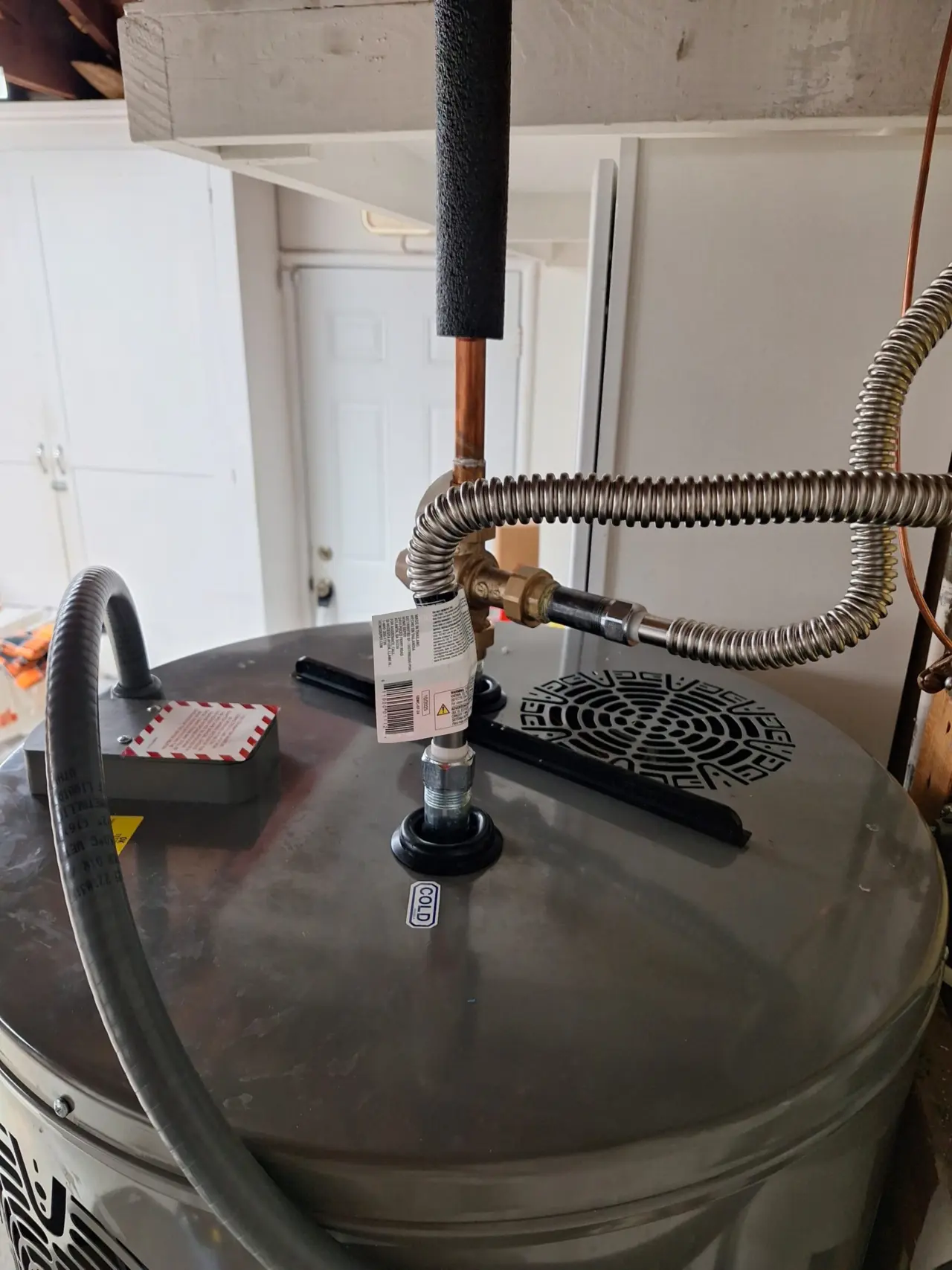 Top of the new Rheem heat pump water heater in a San Mateo garage with insulated copper line, brass valve and stainless flex connectors