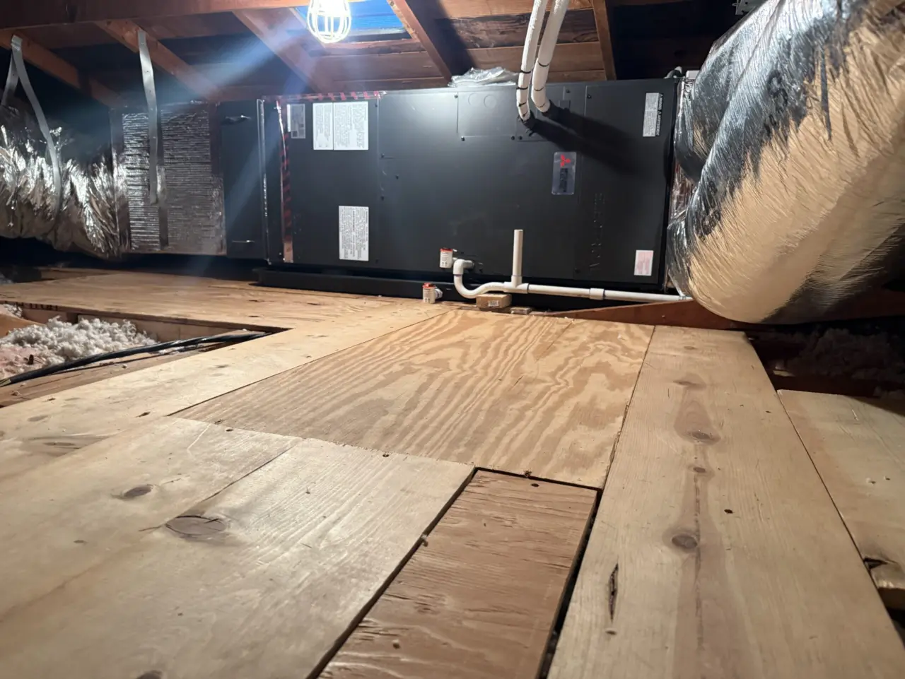 Low-angle view of a new Mitsubishi air handler and supply duct in a Santa Clara attic with plywood decking in front