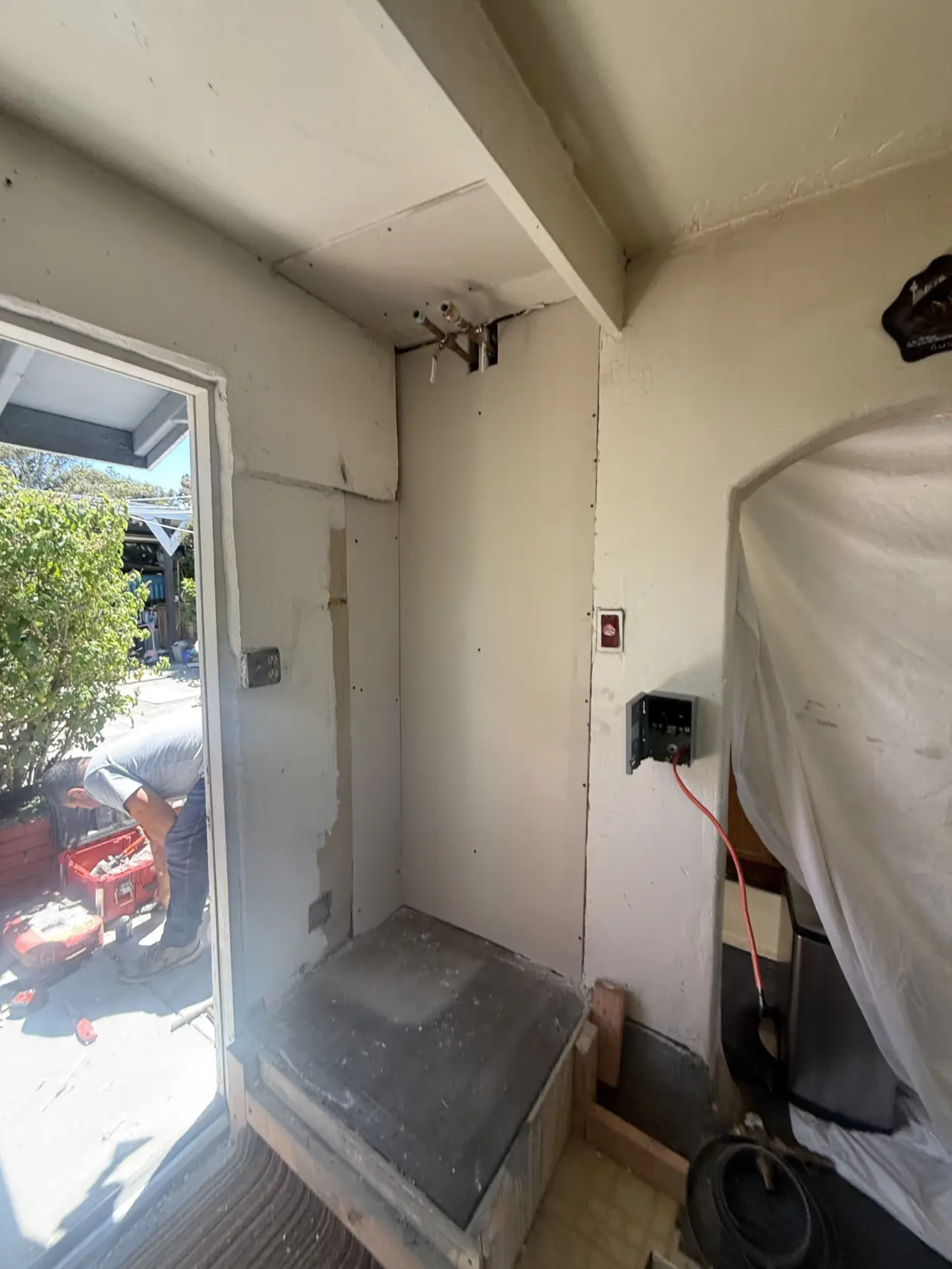 Before: patched wall, raised concrete pad and electrical disconnect ready for a heat pump water heater in South San Francisco